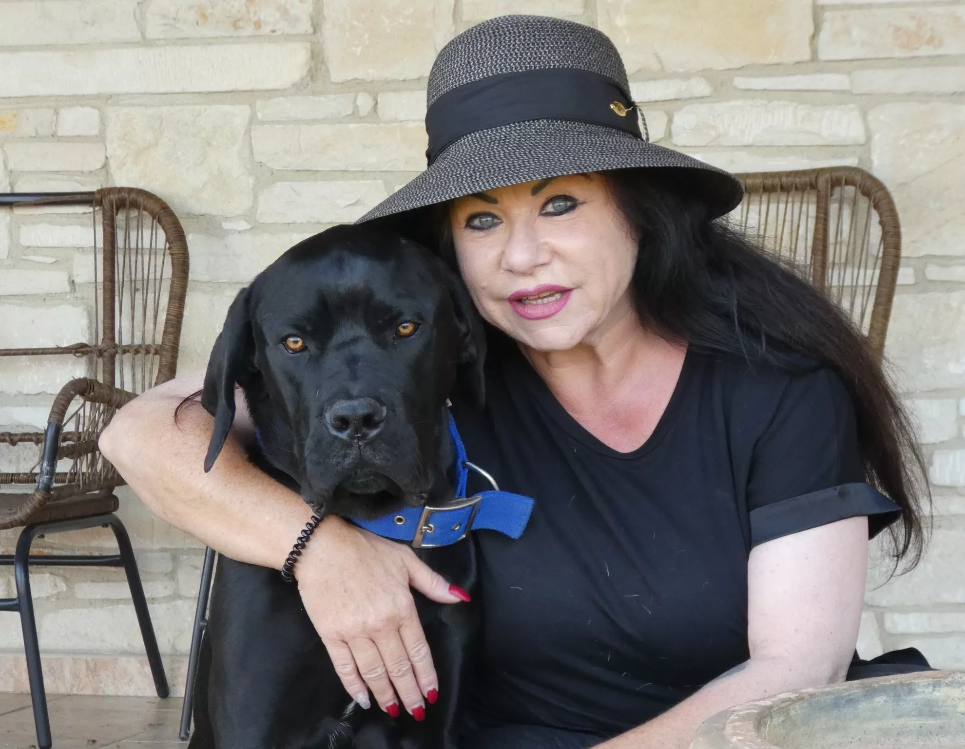 Sabine Kuhn umarmt ihren schwarzen Hund, der ruhig in die Kamera schaut