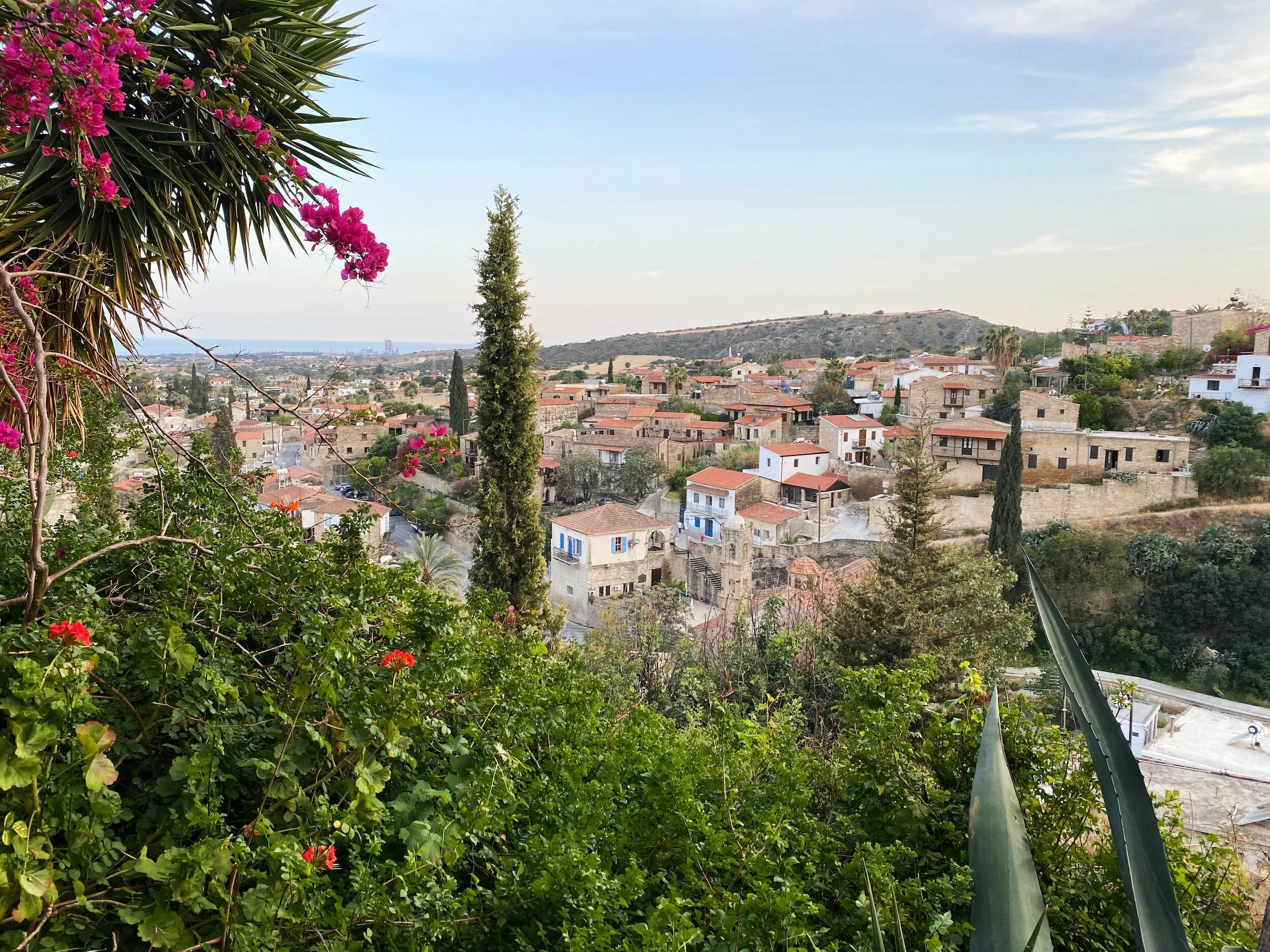 Sabines Dorf auf Zypern: Steinhäuser mit roten Dächern, Zypressen und blühende Bougainvillea, in der Ferne das Meer